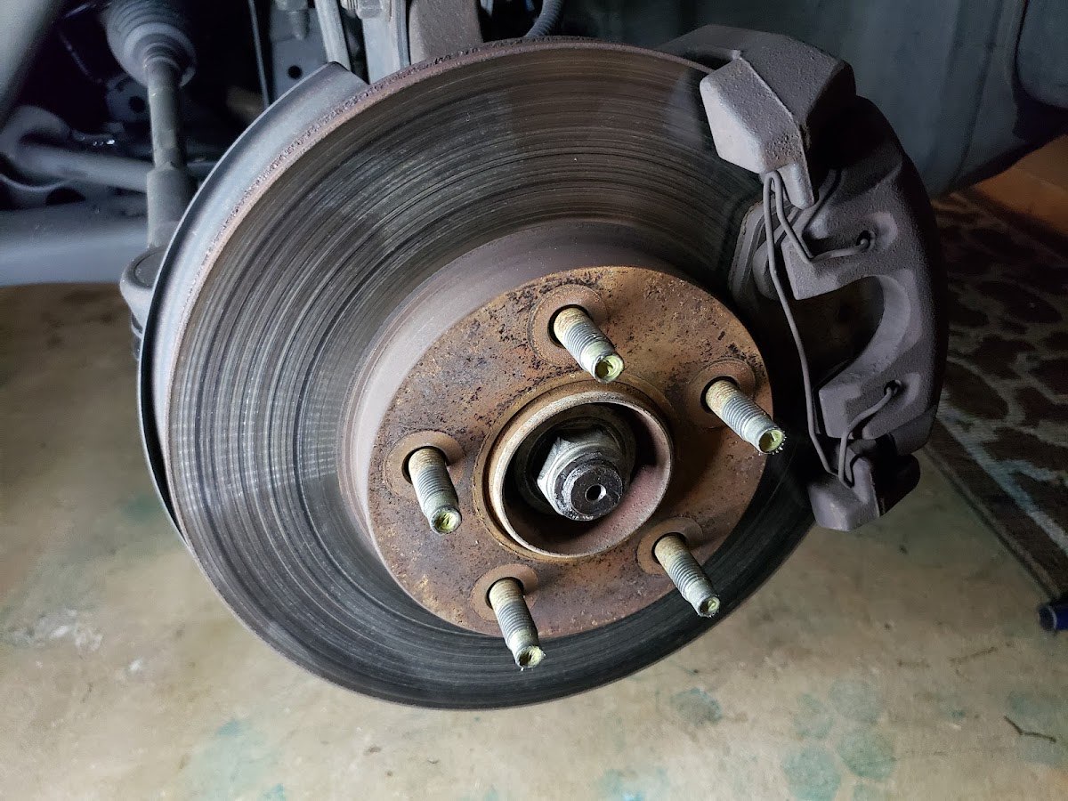 A worn brake rotor and caliper exposed during a mobile brake service